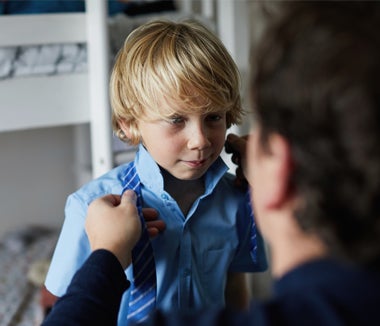 Adult helps a young boy put on a striped tie
